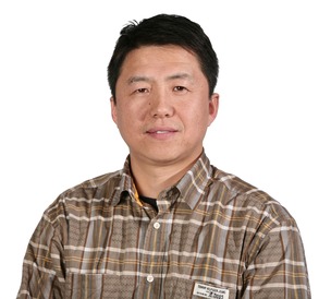 professor wearing a brown plaid button up shirt in front of a white backdrop